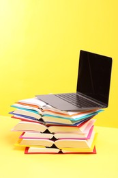 Photo of Stack of colorful books and laptop on yellow background