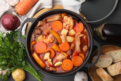 Photo of Tasty homemade stew with vegetables and bread on grey wooden table, flat lay