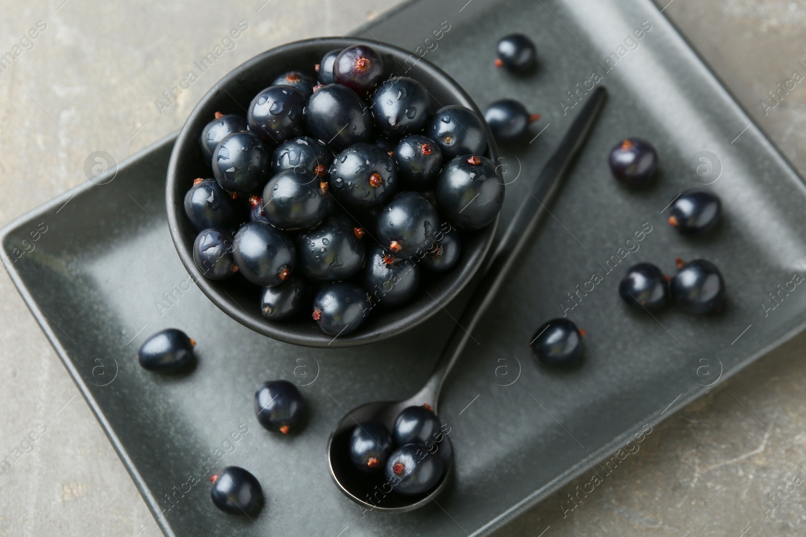 Photo of Ripe black currants with water drops on grey table, above view