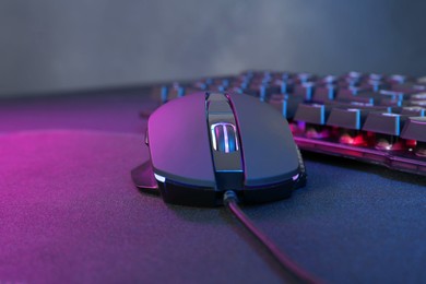 Photo of Computer mouse and RGB keyboard in neon lights on dark background, closeup