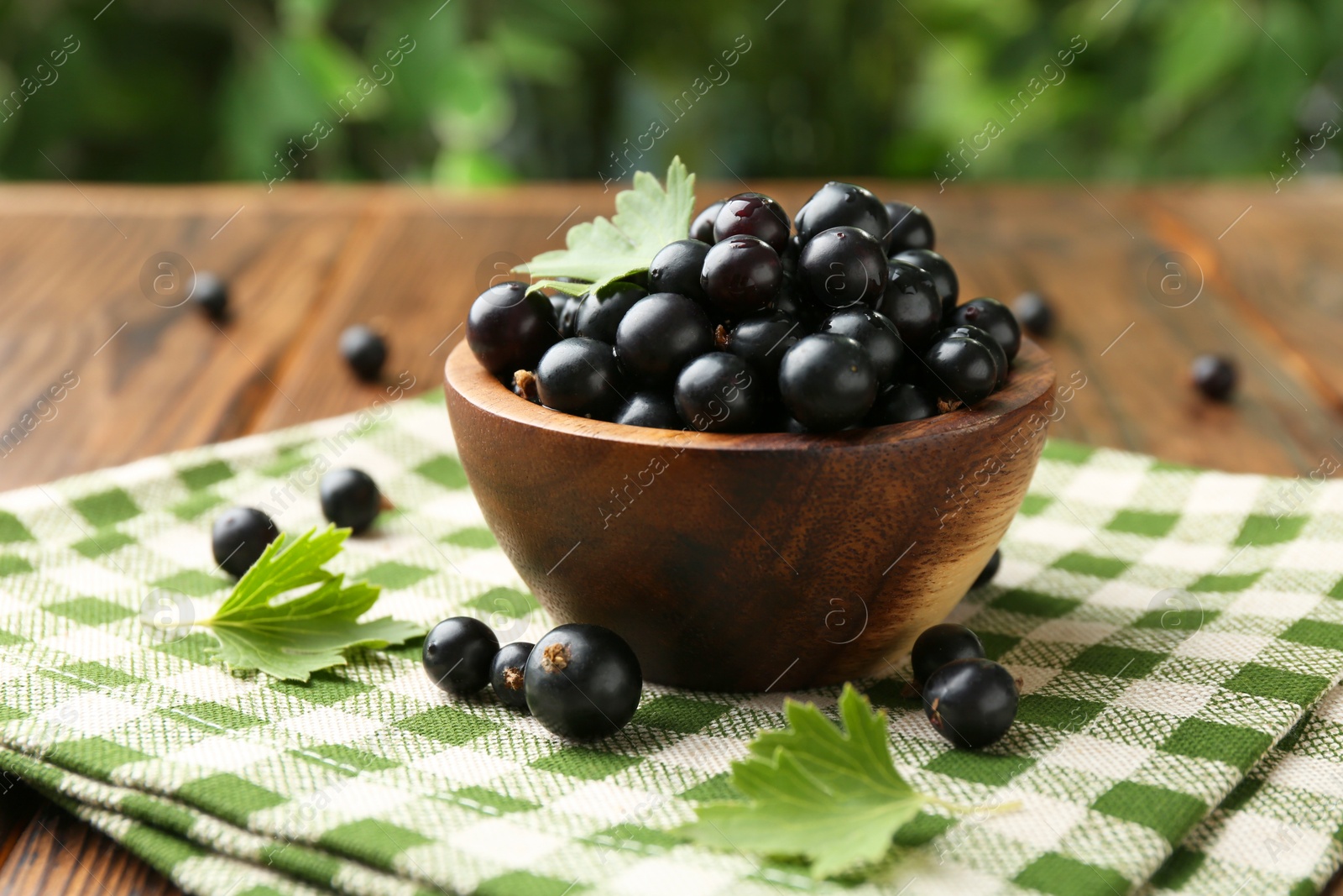 Photo of Ripe black currants and leaves in bowl on wooden table