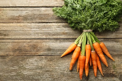 Photo of Bunch of tasty ripe juicy carrots on wooden table, top view. Space for text