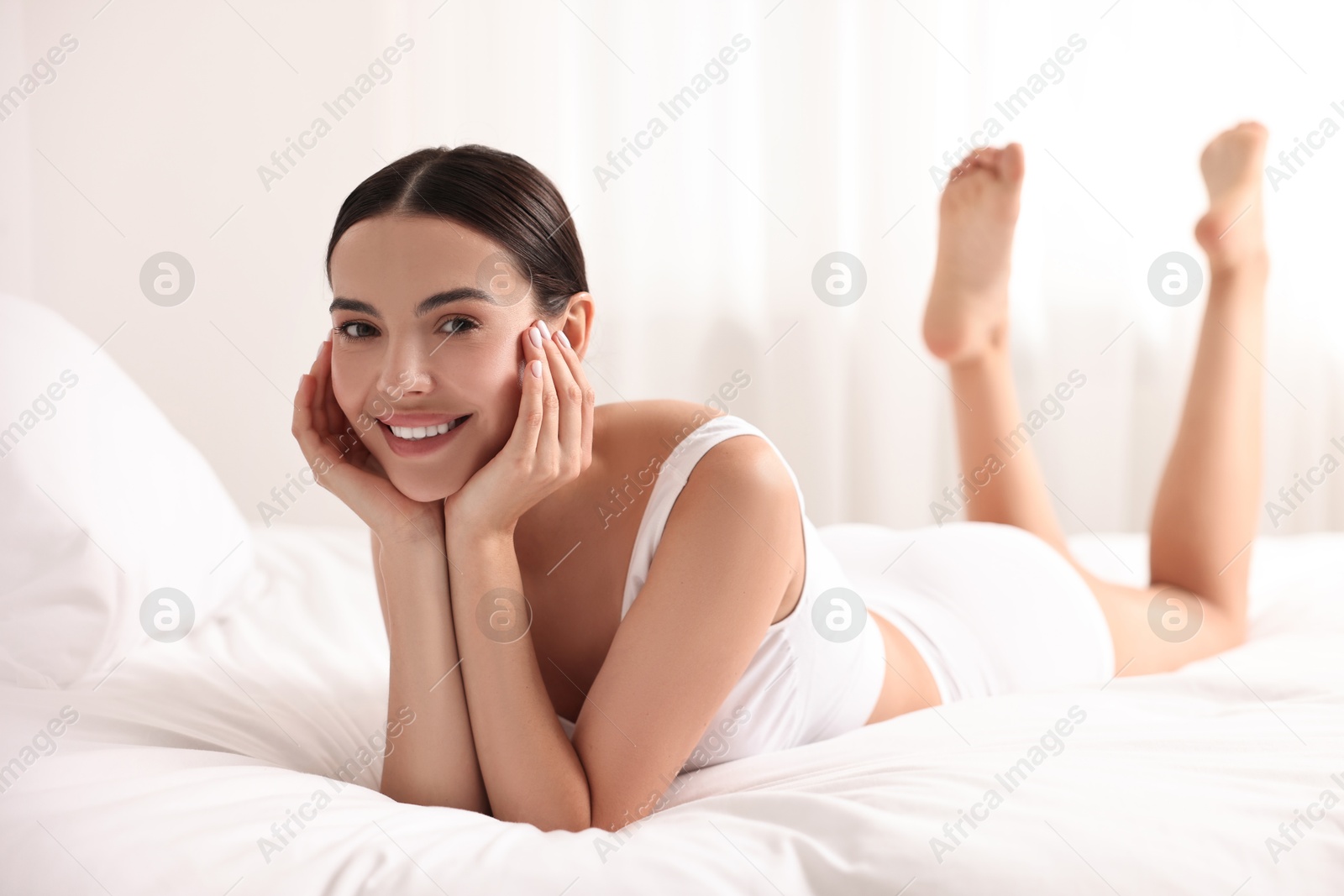 Photo of Smiling woman with perfect skin in underwear on bed. Body care