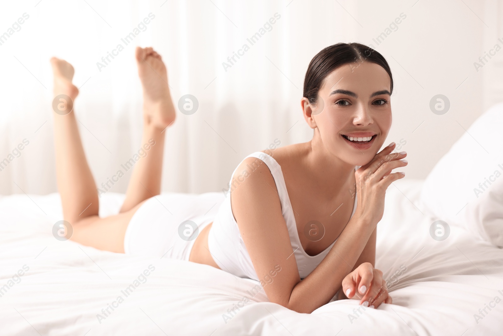 Photo of Smiling woman with perfect skin in underwear on bed. Body care