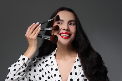 Photo of Beautiful makeup. Smiling woman with brushes on grey background