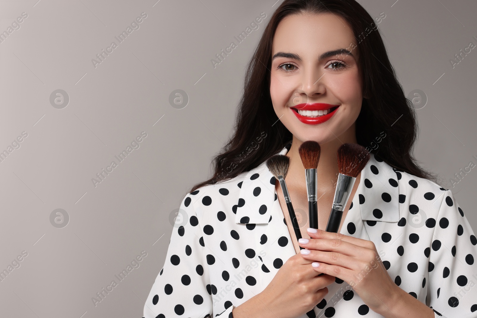 Photo of Beautiful makeup. Smiling woman with brushes on light grey background, space for text