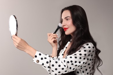 Photo of Beautiful woman with mirror applying makeup on light grey background