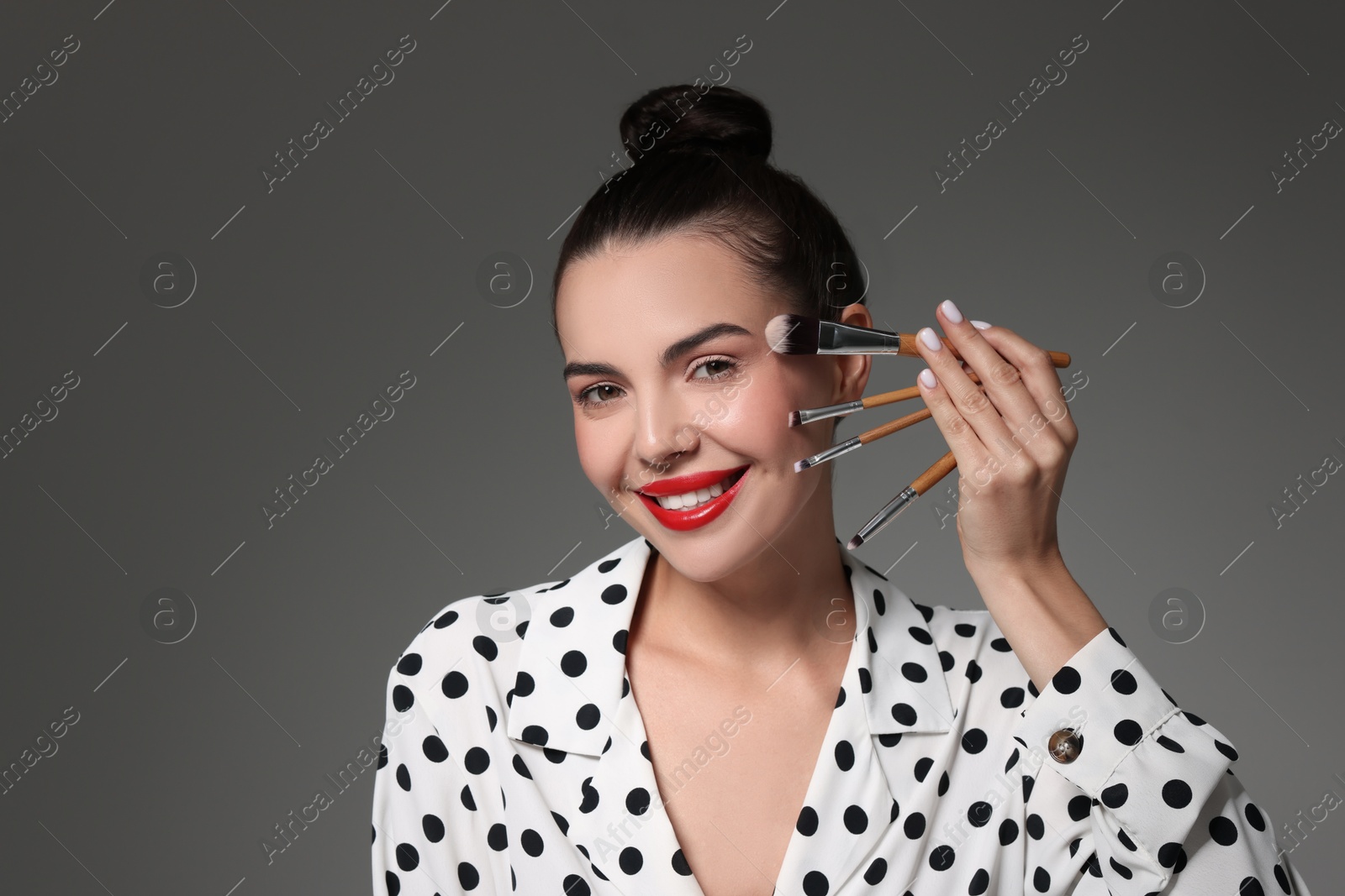 Photo of Beautiful makeup. Smiling woman with brushes on grey background, space for text