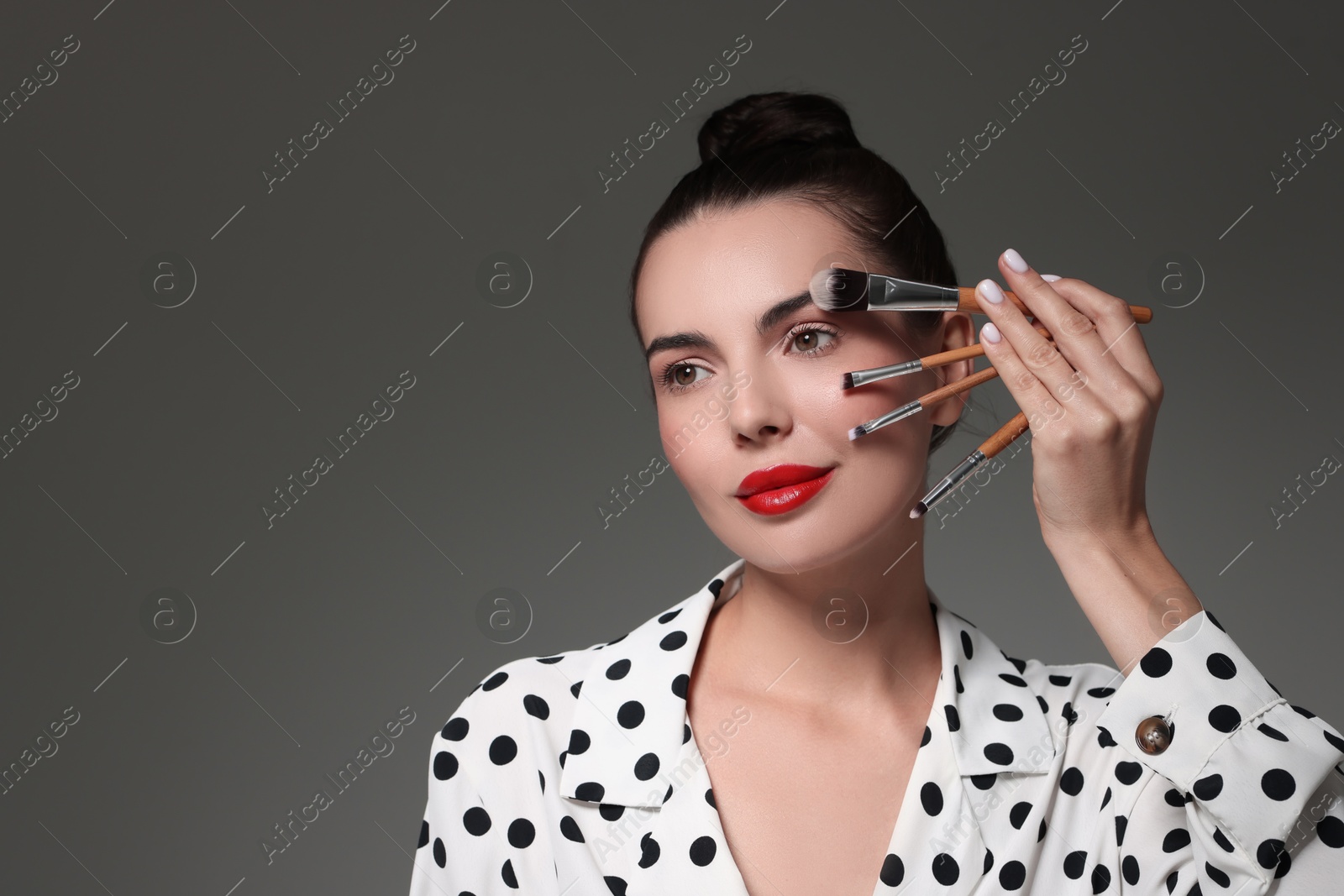 Photo of Beautiful makeup. Attractive woman with brushes on grey background, space for text