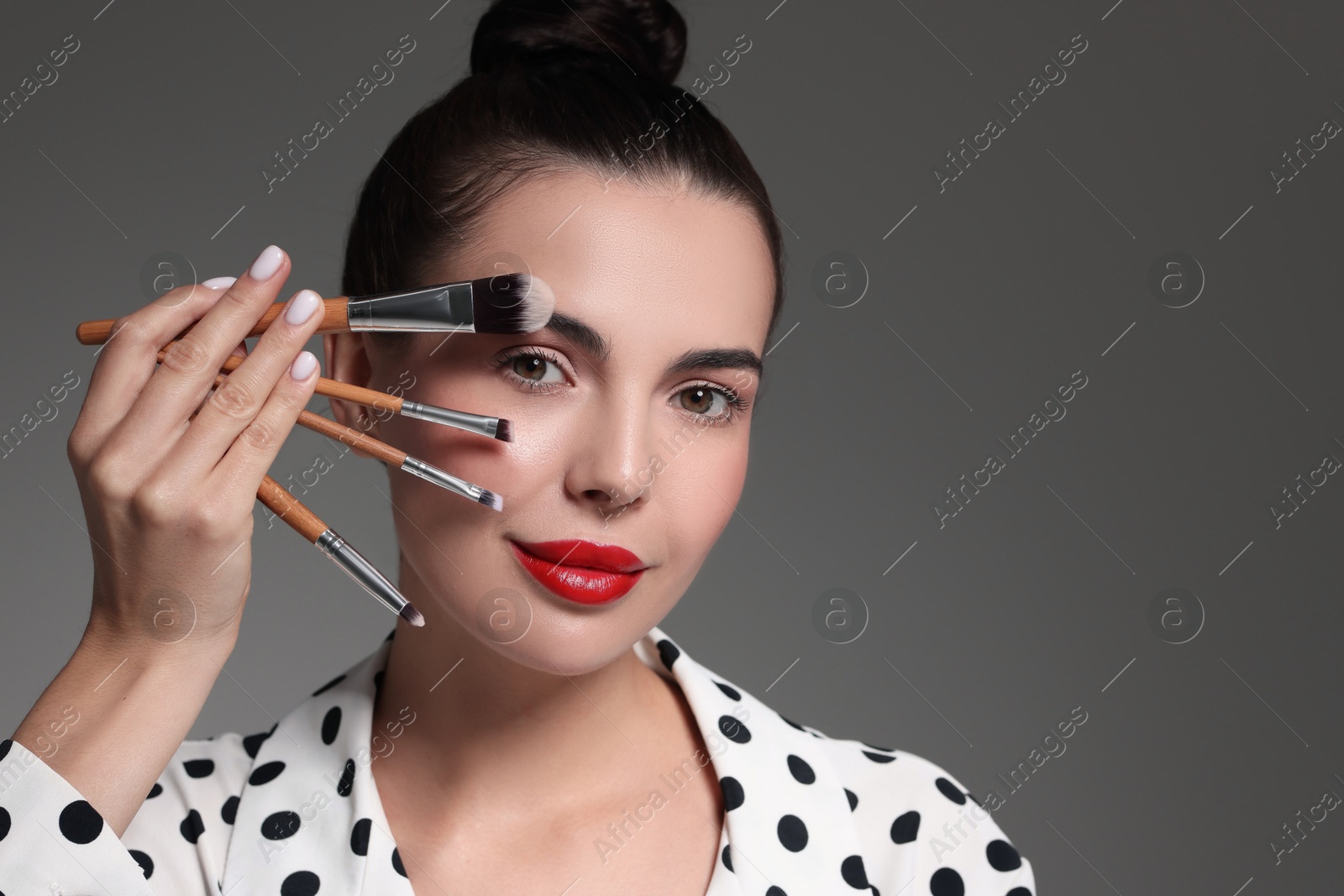 Photo of Beautiful makeup. Attractive woman with brushes on grey background, space for text