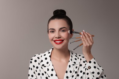 Beautiful makeup. Smiling woman with brushes on grey background