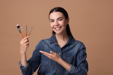 Beautiful makeup. Attractive woman with brushes on beige background