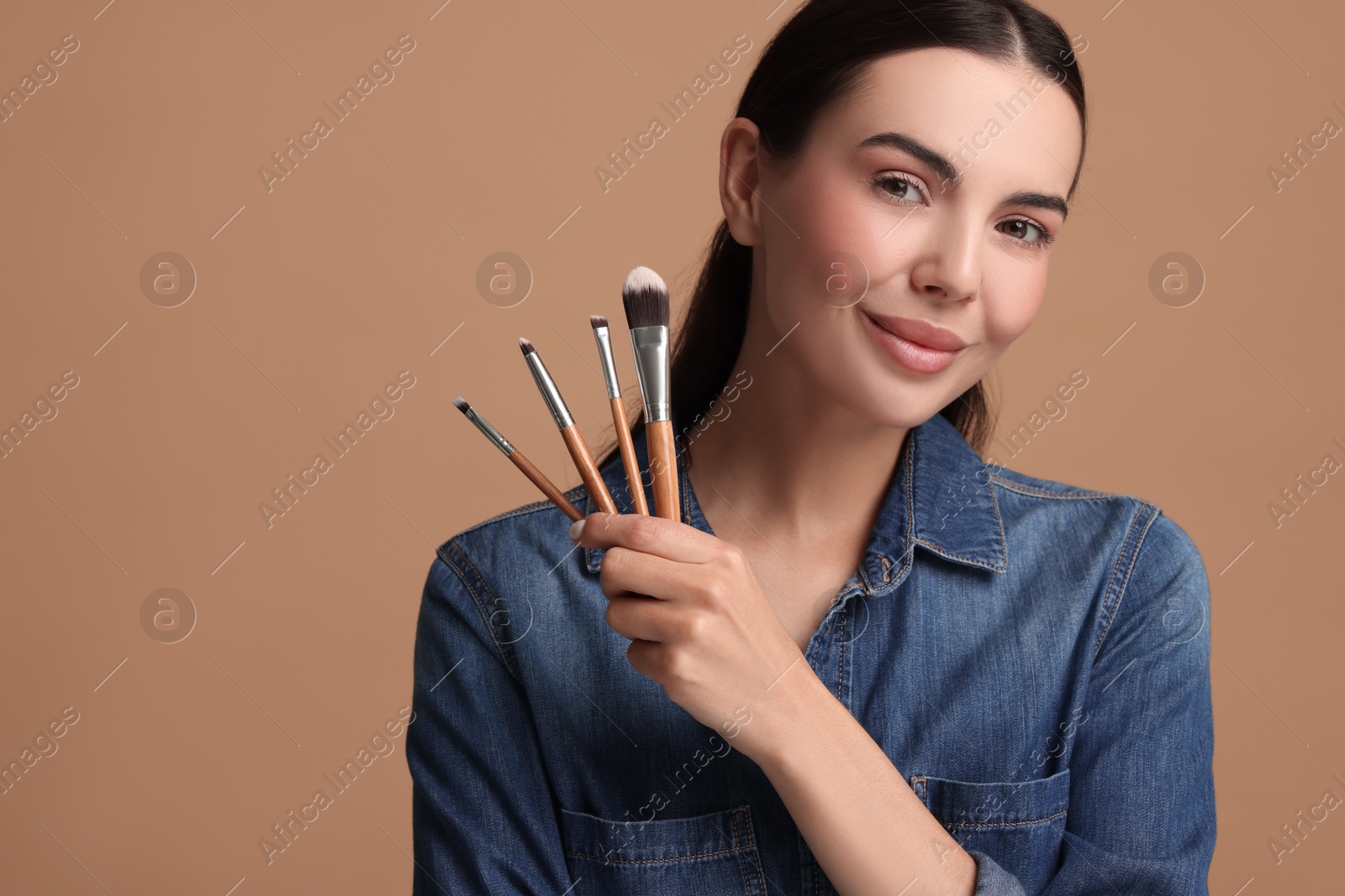 Photo of Beautiful makeup. Attractive woman with brushes on beige background, space for text