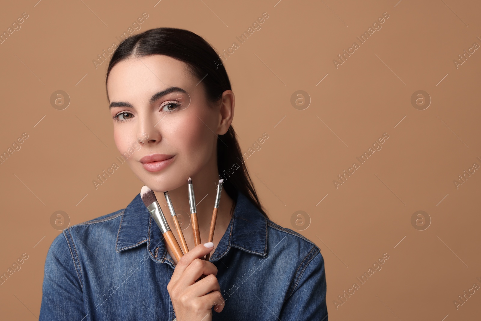 Photo of Beautiful makeup. Attractive woman with brushes on beige background, space for text