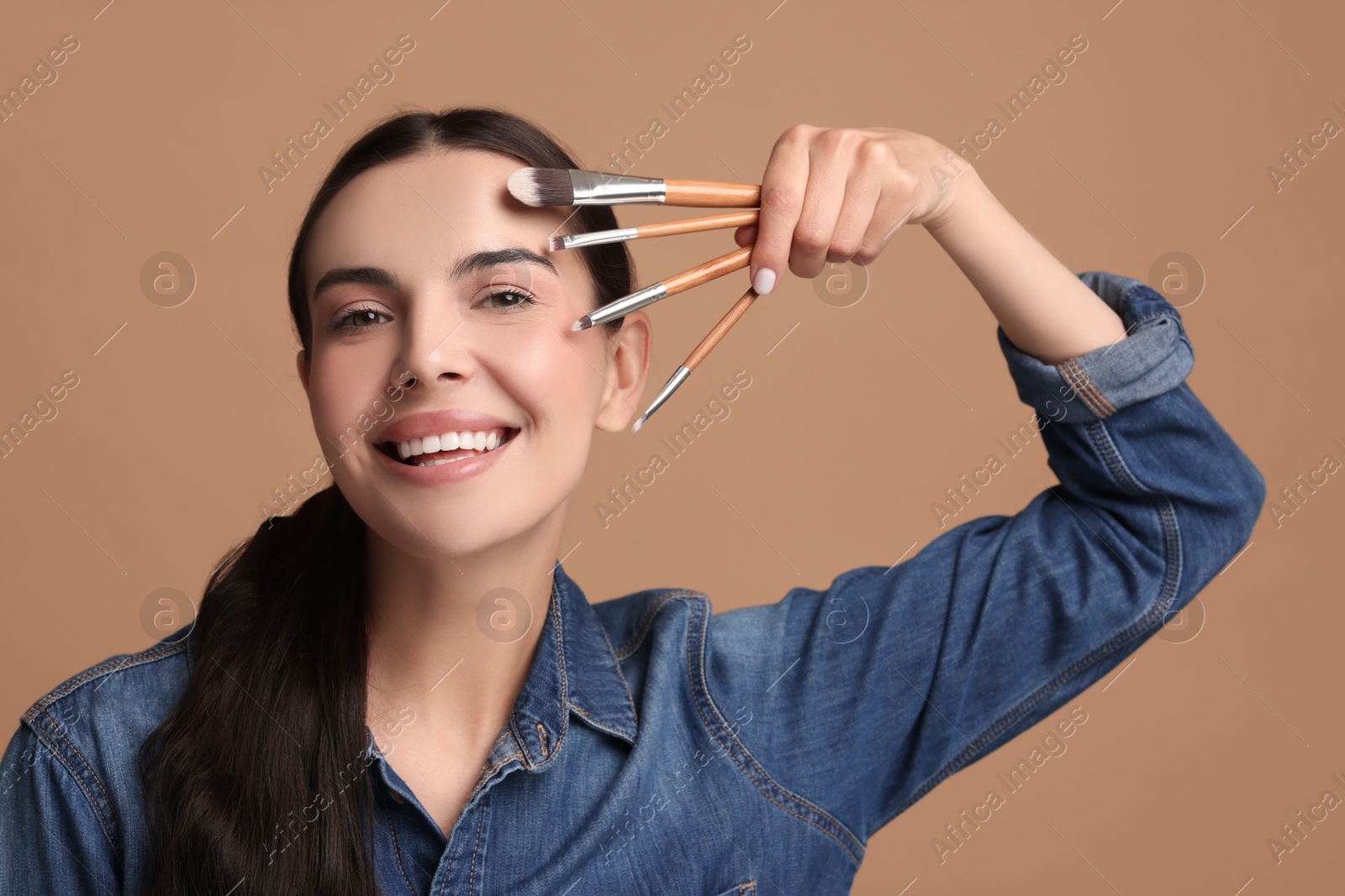 Photo of Beautiful makeup. Smiling woman with brushes on beige background