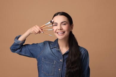 Photo of Beautiful makeup. Smiling woman with brushes on beige background