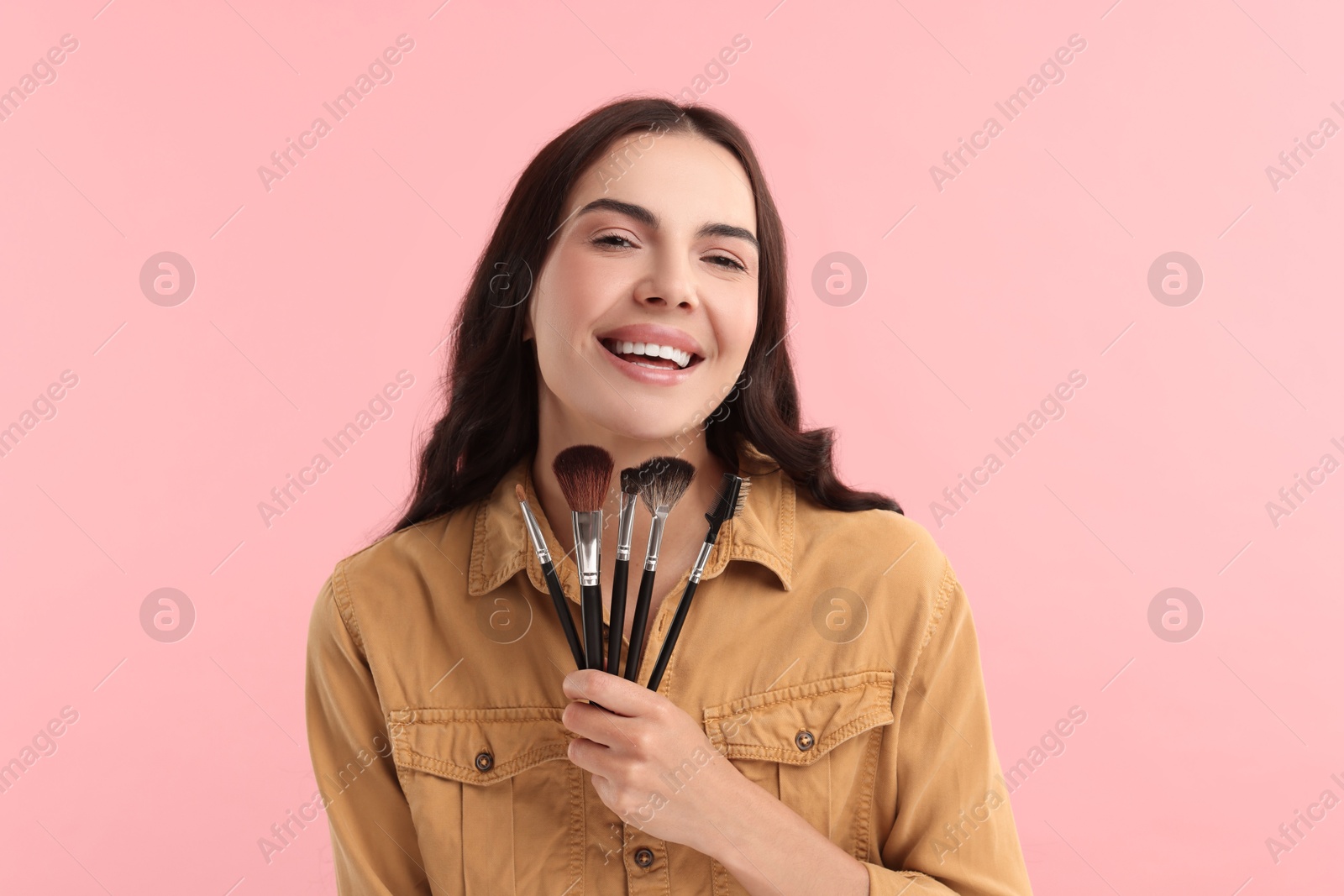 Photo of Smiling woman with beautiful makeup holding brushes on pink background