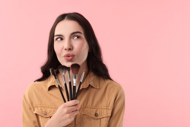 Photo of Attractive woman with beautiful makeup holding brushes on pink background. Space for text