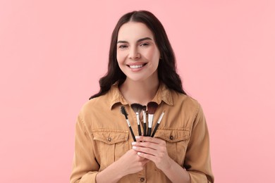 Beautiful makeup. Smiling woman with brushes on pink background