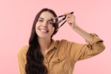 Beautiful makeup. Smiling woman with brushes on pink background