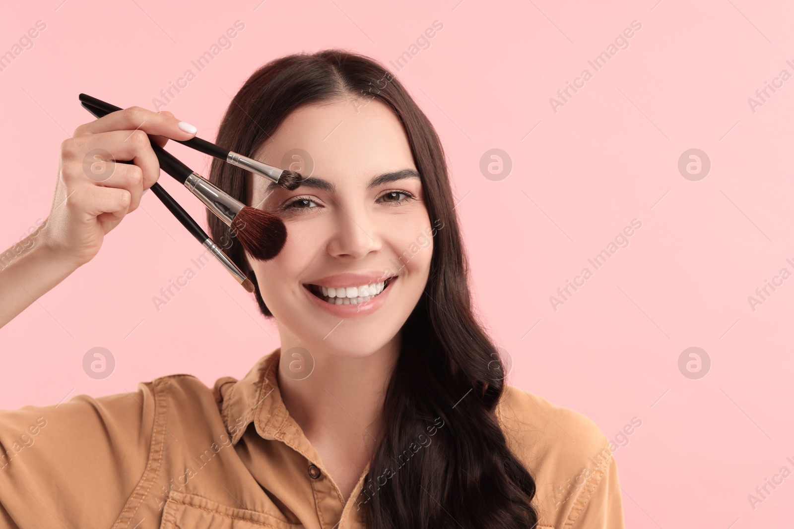 Photo of Beautiful makeup. Smiling woman with brushes on pink background, space for text