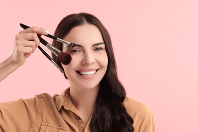 Photo of Beautiful makeup. Smiling woman with brushes on pink background, space for text