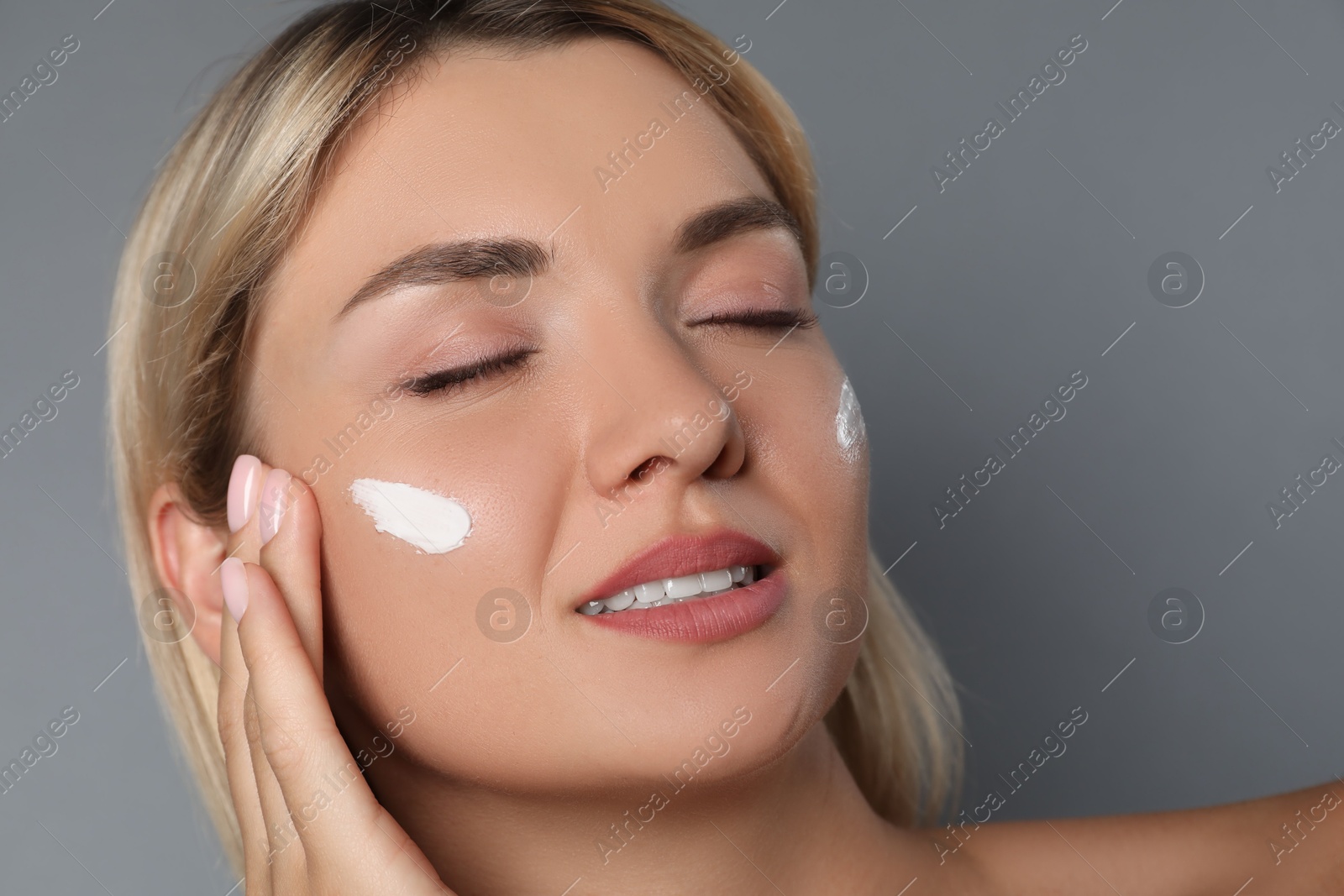 Photo of Beautiful woman with cream on her face against grey background, closeup