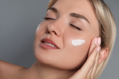 Beautiful woman with cream on her face against grey background, closeup