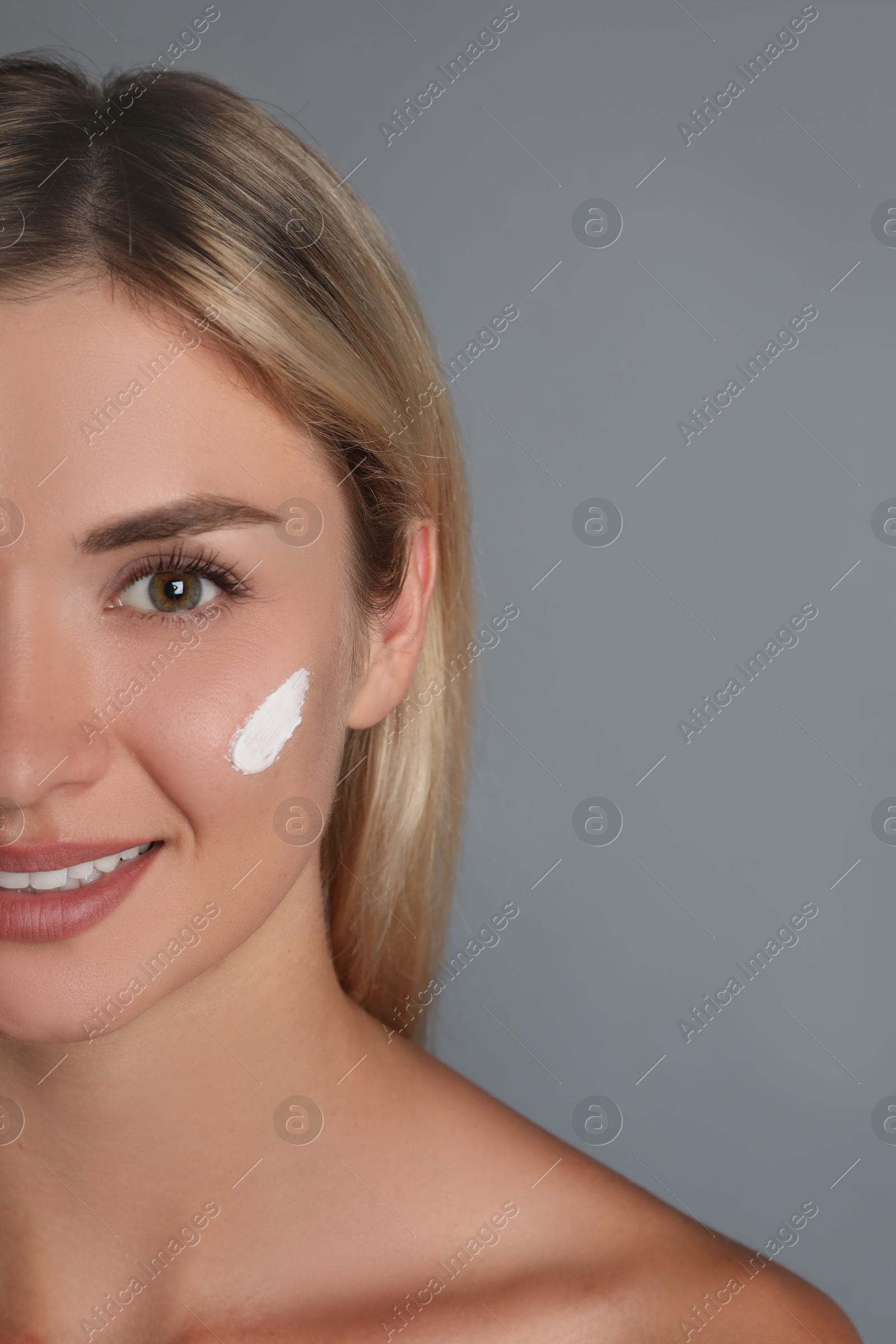 Photo of Beautiful woman with cream on her face against grey background, closeup