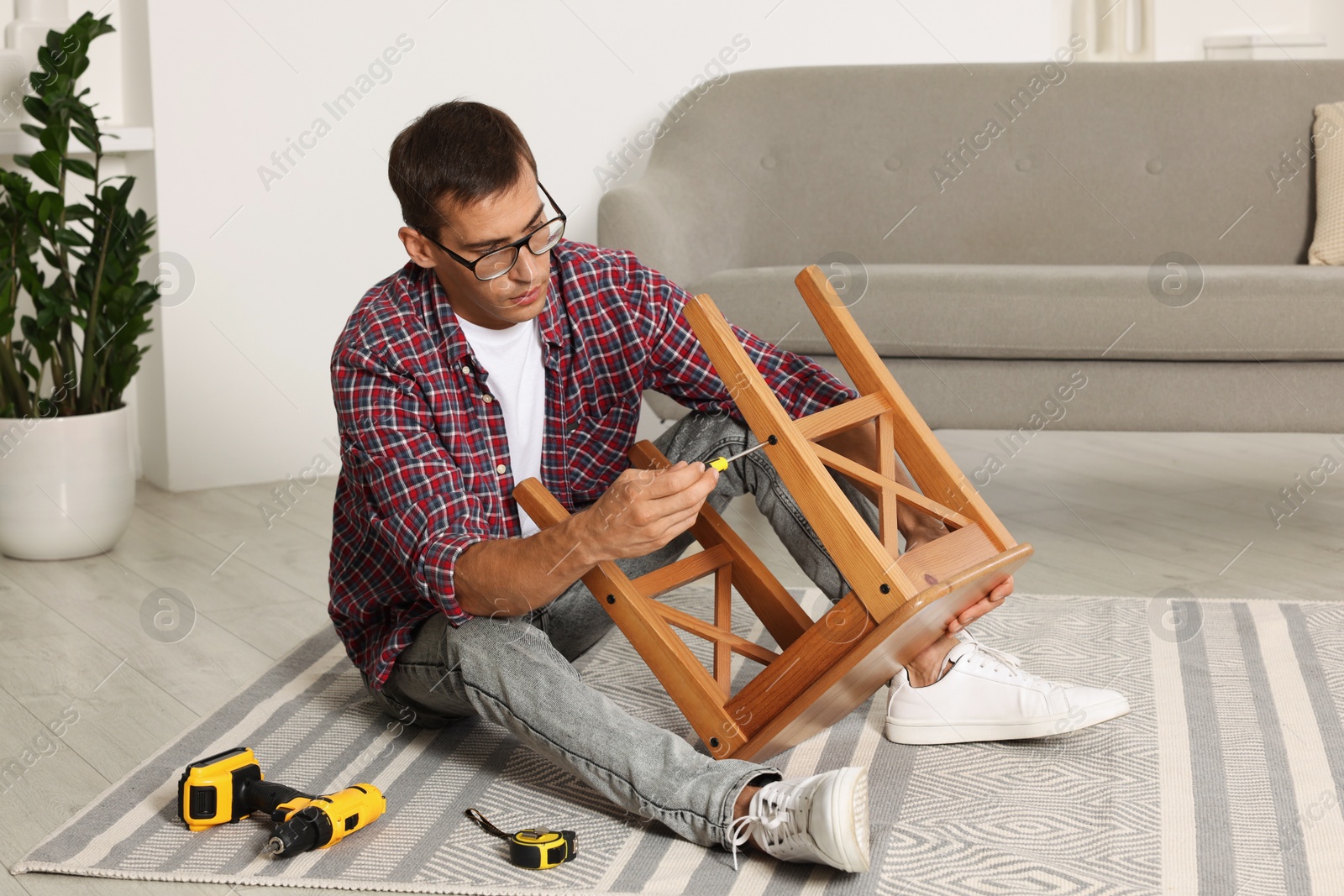 Photo of Man repairing wooden stool with screwdriver indoors