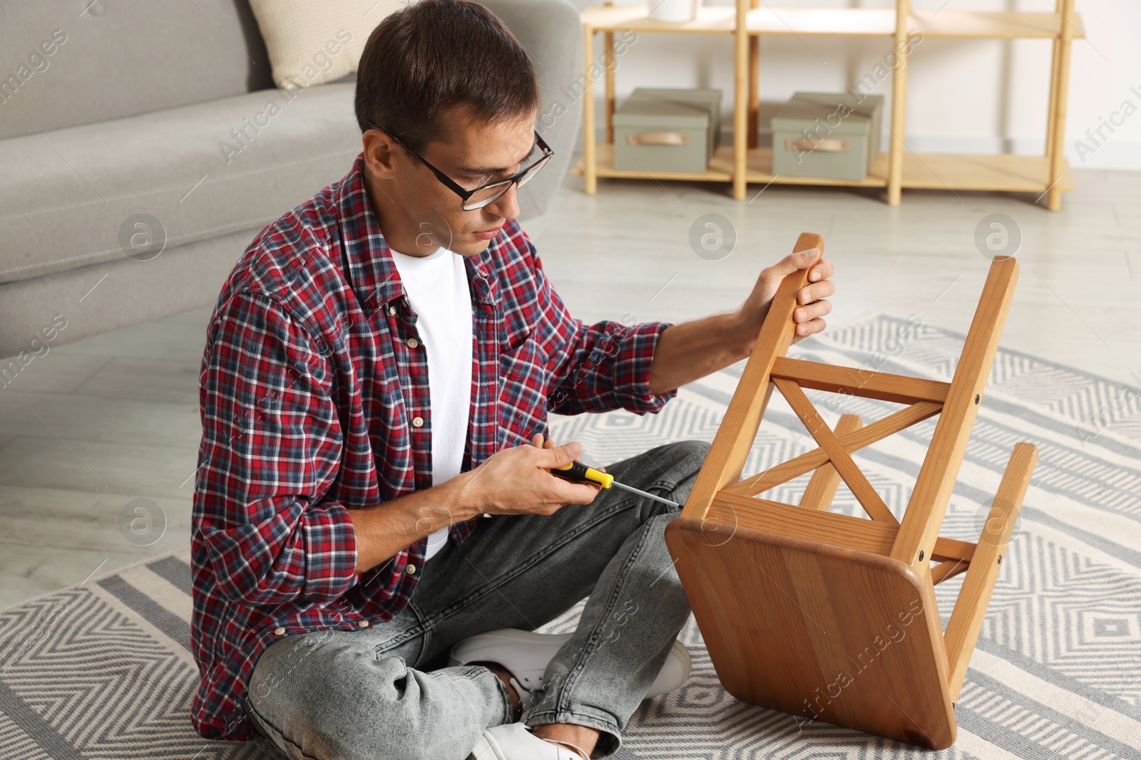 Photo of Man repairing wooden stool with screwdriver indoors