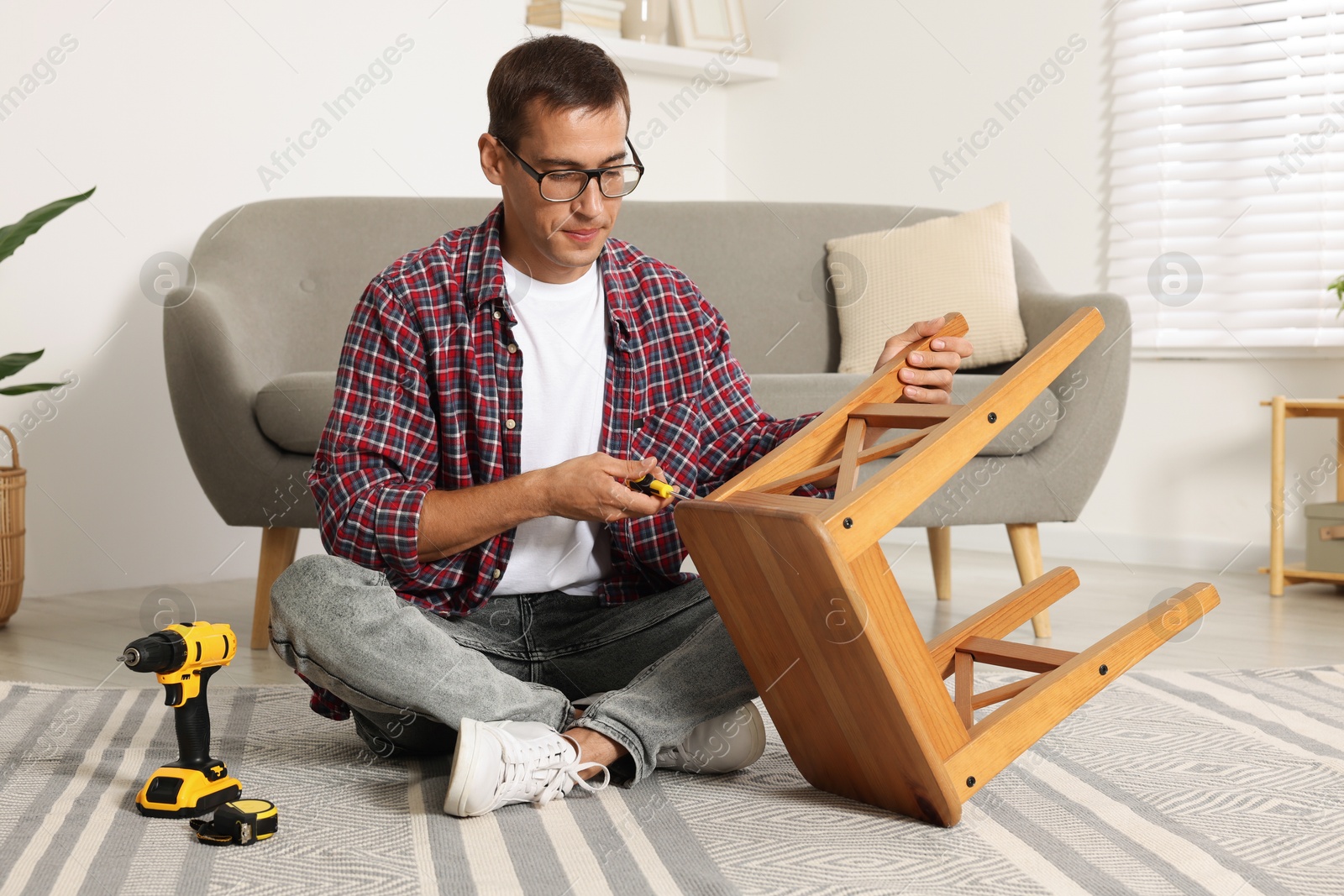 Photo of Man repairing wooden stool with screwdriver indoors