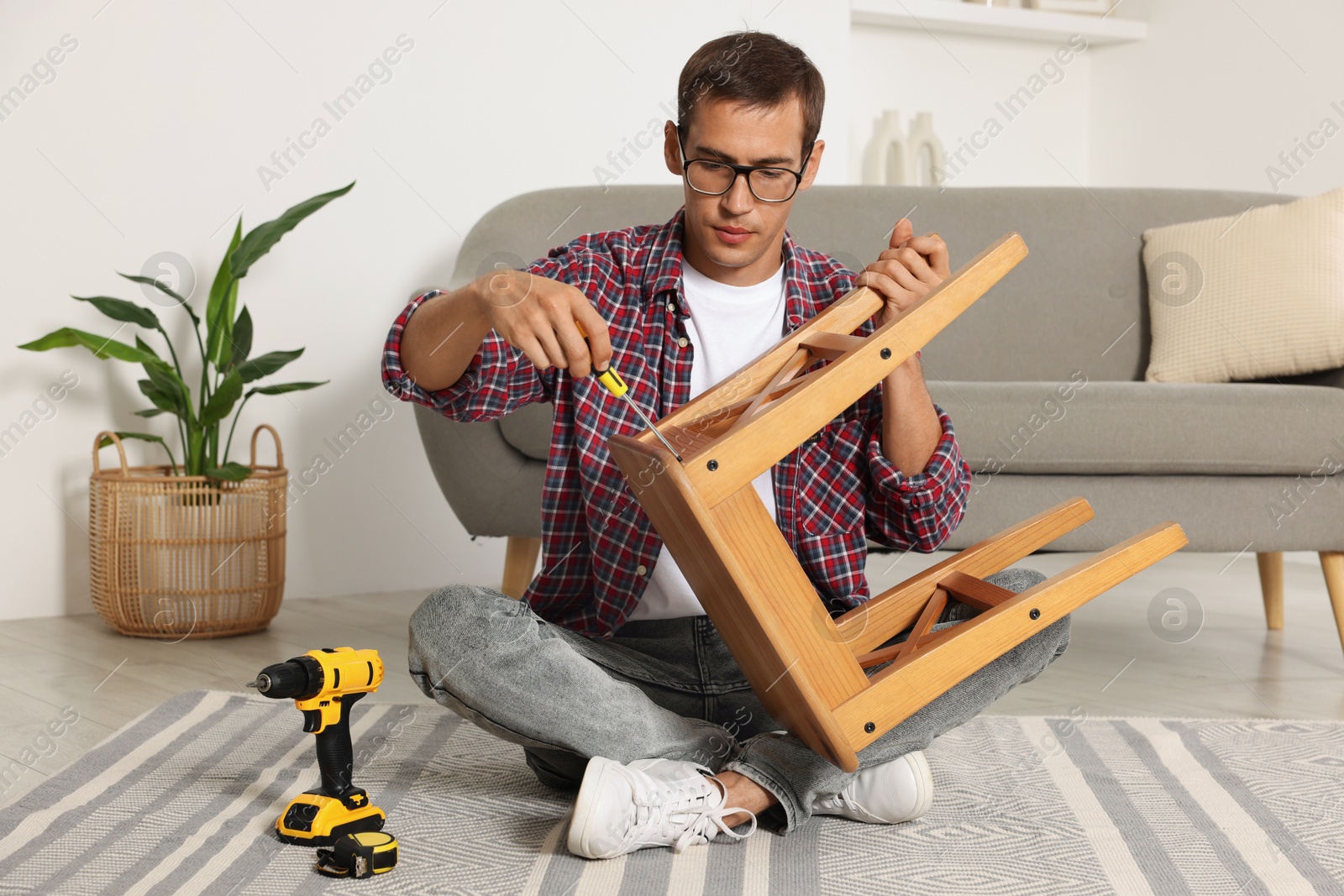 Photo of Man repairing wooden stool with screwdriver indoors