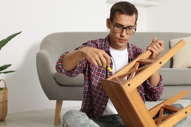 Man repairing wooden stool with screwdriver indoors