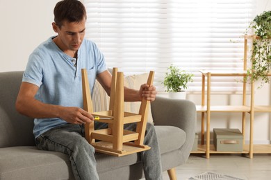 Photo of Man repairing wooden stool with screwdriver indoors