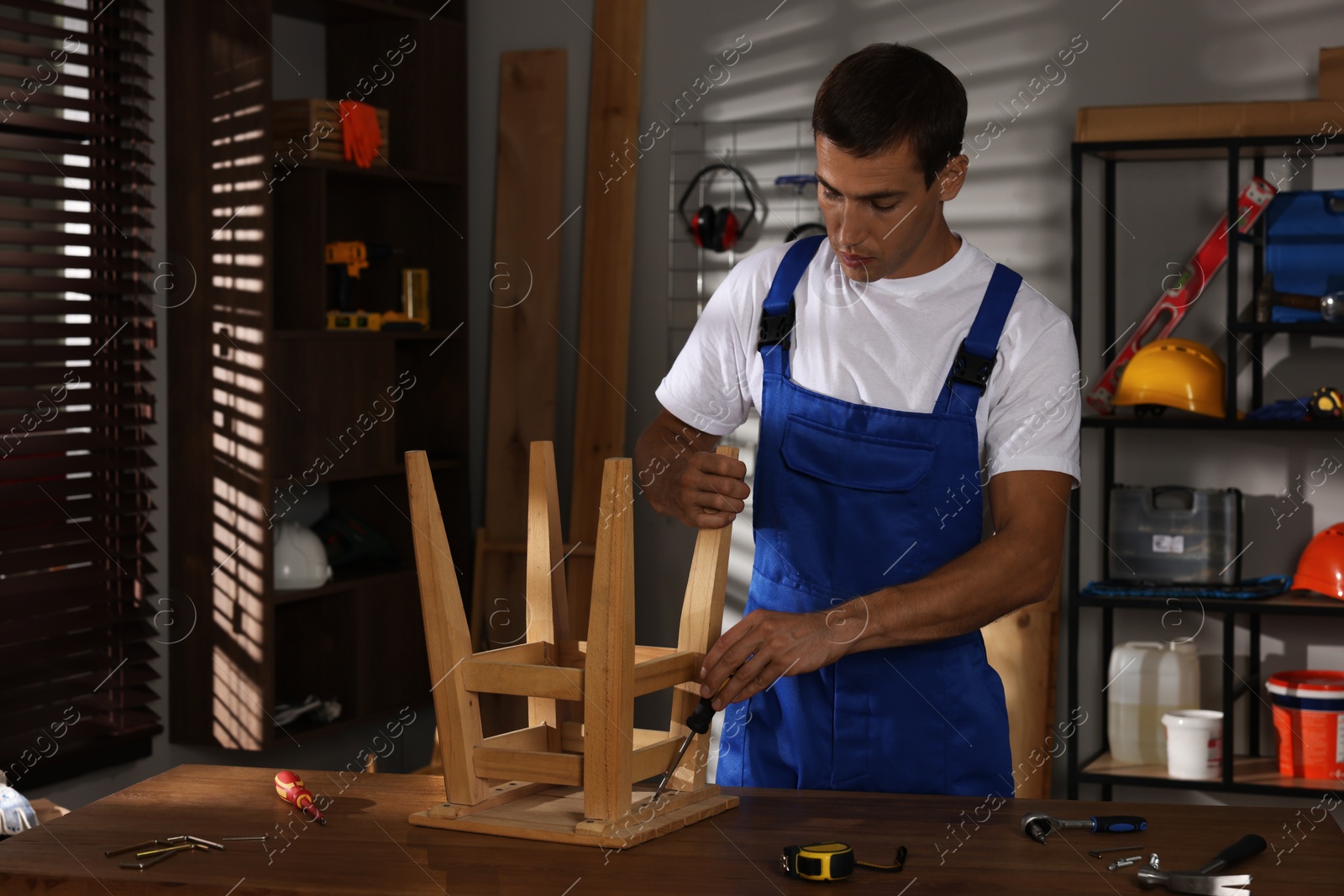 Photo of Man repairing wooden stool with screwdriver indoors