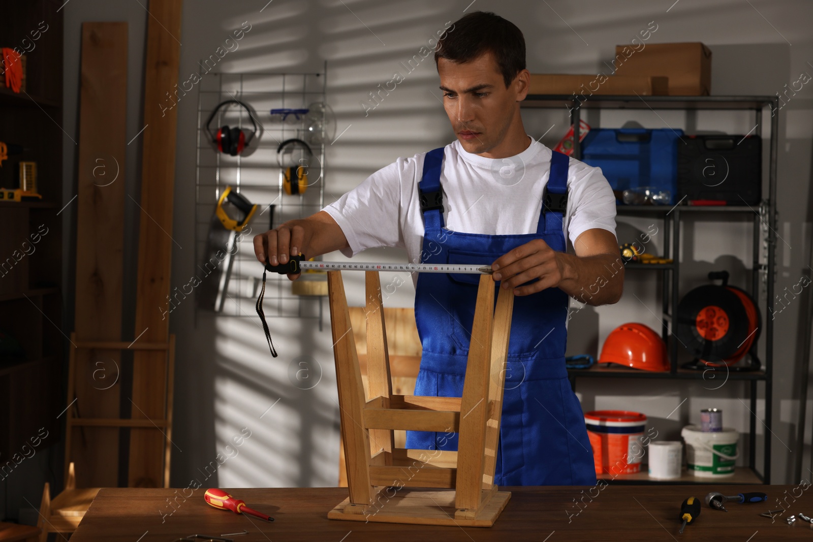 Photo of Man using tape measure while repairing wooden stool indoors