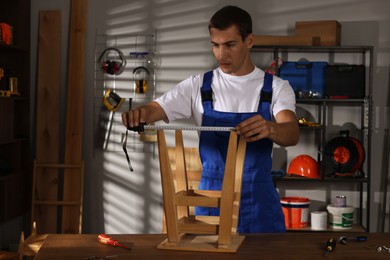 Man using tape measure while repairing wooden stool indoors