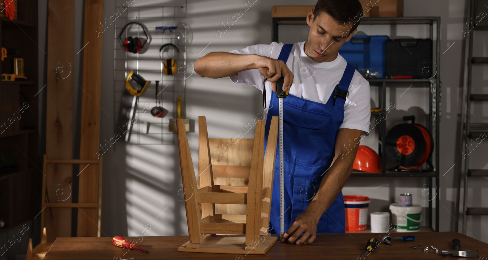 Photo of Man using tape measure while repairing wooden stool indoors