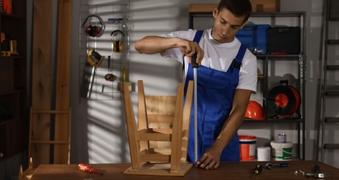 Man using tape measure while repairing wooden stool indoors