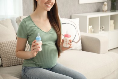 Expecting twins. Pregnant woman holding two bottles of milk at home, closeup. Space for text