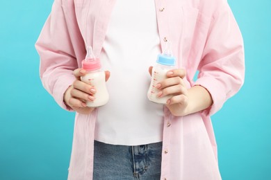 Expecting twins. Pregnant woman holding two bottles with milk on light blue background, closeup