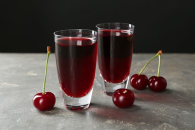 Photo of Delicious cherry liqueur in shot glasses and fresh berries on grey table