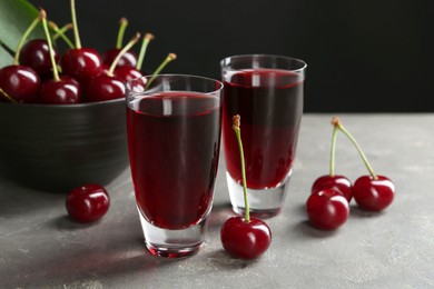 Delicious cherry liqueur in shot glasses and fresh berries on grey table