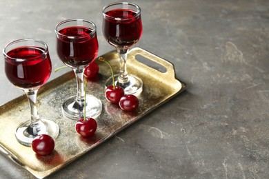 Photo of Delicious cherry liqueur in glasses and fresh berries on grey table, space for text