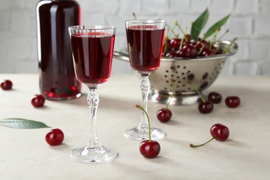 Delicious cherry liqueur in glasses and fresh berries on light grey table