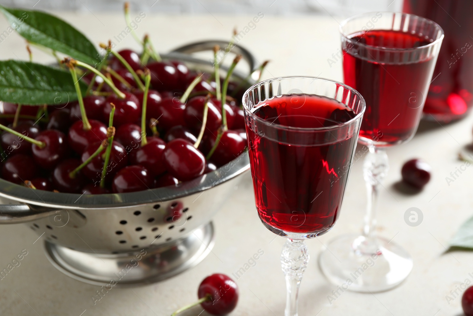 Photo of Delicious cherry liqueur in glasses and fresh berries on light grey table