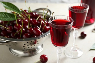 Photo of Delicious cherry liqueur in glasses and fresh berries on light grey table