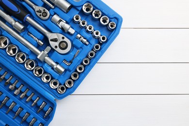 Auto mechanic's tools in plastic box on white wooden table, top view. Space for text