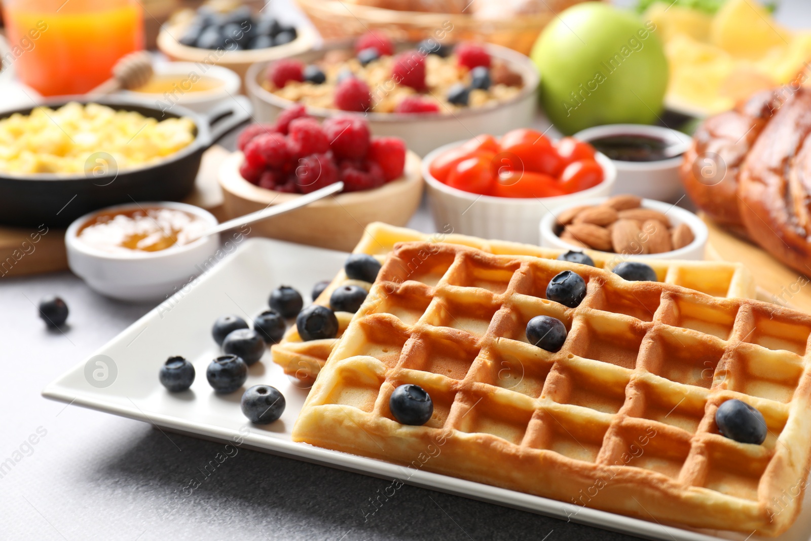 Photo of Tasty breakfast. Belgian waffles, blueberries and other food on grey textured table, closeup